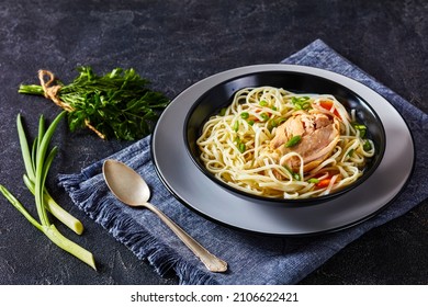 Chicken Noodle Soup With Carrots And Scallion In A Black Bowl On A Grey Concrete Table With Spoon, Horizontal View From Above