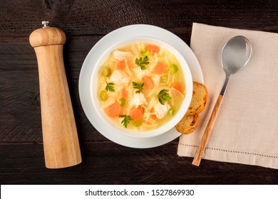 Chicken Noodle Soup, Shot From Above On A Dark Rustic Wooden Background With Toasted Bread And A Pepper Mill