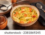 Chicken noodle soup with vegetables, a bowl of healthy broth with a ladle, on a rustic wooden table, winter comfort food