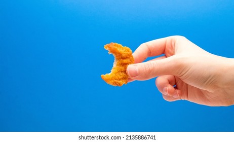 Chicken Nugget With A Bite Taken In Hand On A Blue Background