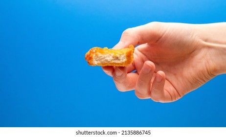 Chicken Nugget On Side With A Bite Taken In Hand On A Blue Background