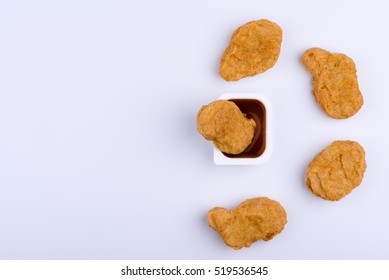 Chicken Nugget Standing In Red Dip Sauce, Surrounded By Four More Chicken Nuggets, Isolated On White Background