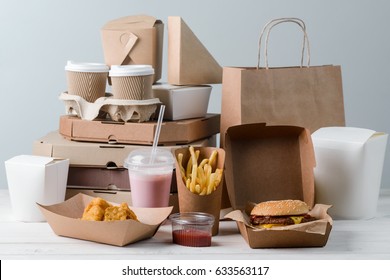 Chicken Nuggets, milkshake, sauce, hamburger, French fries, espresso and latte. Pizza boxes and paper bag, light wooden background. Fast food, binge eating. - Shutterstock ID 633563117