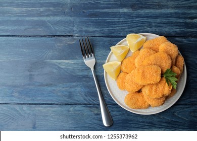 chicken nuggets on a plate with fork with lemon slices on a blue wooden table. top view with space for text