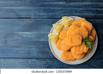 chicken nuggets on a plate with lemon slices on a blue wooden table. top view with space for text
