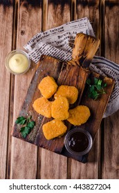 Chicken Nuggets on wooden cutting board with ketchup and sauce, on wooden background