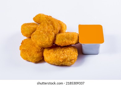 Chicken nuggets stacked with sauce in a plastic container on a white background. Horizontal orientation
