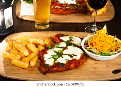 Chicken Parma With Chips And Salad On A Wooden Plate With Beer And Wine 