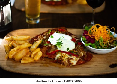 Chicken Parma With Chips And Salad On A Wooden Plate With Beer And Wine 