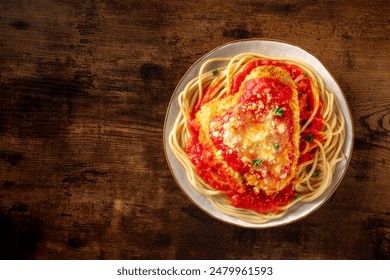 Chicken Parmesan, Italian pasta dish. Breaded chicken breast with cheese and spaghetti with tomato sauce, shot from above on a wooden table with copy space - Powered by Shutterstock