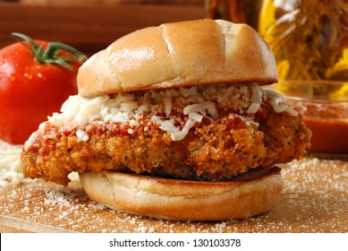 Chicken Parmesan Sandwich (seasoned And Fried Chicken Breast With Tomato Basil Marinara Sauce And Mozzarella On A Grilled Bun) With Ingredients And Cooking Oil In Background.  Macro With Shallow Dof.