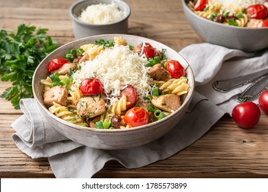Chicken pasta salad with roasted and sun-dried tomatoes, topped with green onion slices and grated cheese on wooden background - Shutterstock ID 1785573899