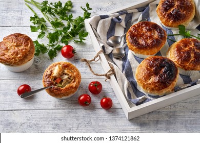 Chicken Pot Pie With Creamy Filling Of Cream, Carrot, Celery, Peas, Chicken Breast, With Puff Pastry Crust On Top, Served In The Individual Ramekin, On A White Wooden Table