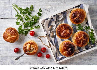 Chicken Pot Pie With Creamy Filling Of Cream, Carrot, Celery, Peas, Chicken Breast, Cream With Puff Pastry Crust, Served In The Individual Ramekin, Top View, Flat Lay On A White Wooden Table