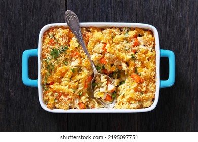 Chicken Pot Pie Fusilli pasta Bake with celery, corn, green peas, carrots , topped with panko breadcrumbs in baking dish on dark wood table, horizontal view from above, flat lay, close-up