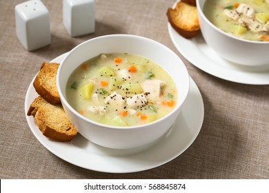 Chicken and potato chowder soup with green bell pepper and carrot in bowls with toasted bread slices on the side, photographed with natural light (Selective Focus, Focus one third into the first soup)