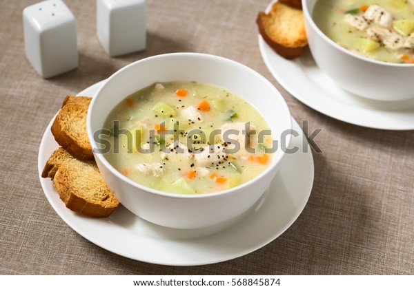 Chicken and potato chowder soup with green bell\
pepper and carrot in bowls with toasted bread slices on the side,\
photographed with natural light (Selective Focus, Focus one third\
into the first soup)