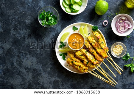 Chicken satay with peanut sauce. Grilled chicken skewers served with peanut dipping sauce. Tasty meal for dinner or party appetizers. Blue stone background with free text space. Top view, flat lay
