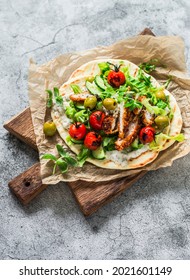 Chicken schnitzel greek gyros with lettuce, tzatziki sauce, roasted tomatoes, cucumbers, olives on a cutting board on a light background, top view       