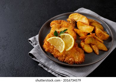 chicken schnitzel with idaho potatoes on a dark plate and a black background, horizontally, space for text on the left