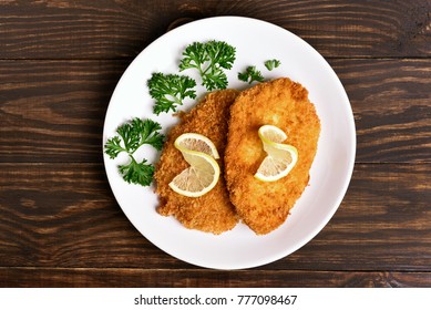 Chicken schnitzel on plate over wooden background. Top view, flat lay