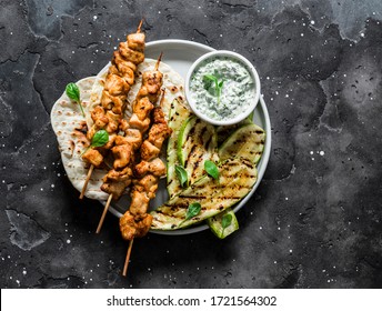 Chicken skewers souvlaki, grilled zucchini, tortillas and tzadziki sauce - delicious greek style lunch on a dark background, top view               
