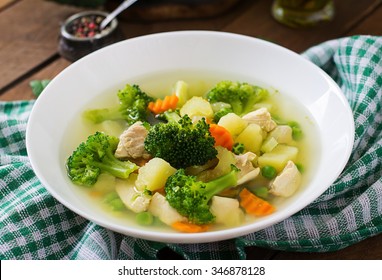 Chicken soup with broccoli, green peas, carrots and celery in a white bowl on a wooden background in rustic style