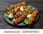 chicken souvlaki with parsley and lime wedges on black plate on dark wooden table, greek cuisine