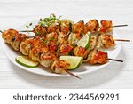 chicken souvlaki with thyme and lime wedges on white plate on white wooden table, landscape view from above