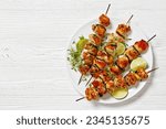 chicken souvlaki with thyme and lime wedges on white plate on white wooden table, horizontal view from above, flat lay, free space