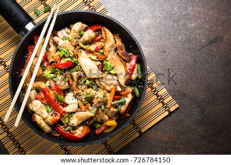 Chicken stir fry with   vegetables soy sause and sesame in the wok. Traditional asian food. Top view wiht copy space on stone table.