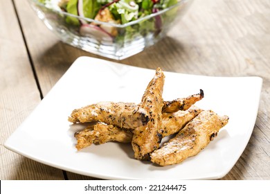 Chicken Strips On A White Plate With A Side Salad On A Wooden Table