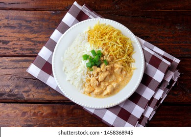 Chicken stroganoff, is a dish originating from Russian cuisine that in Brazil is composed of sour cream with tomato extract, rice and potato chips, on rustic wooden table.