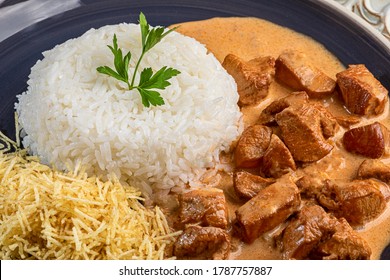 Chicken stroganoff with rice and french fries on a plate, over rustic wooden table.