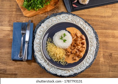 Chicken stroganoff with rice and french fries on a plate, over rustic wooden table. Top view.