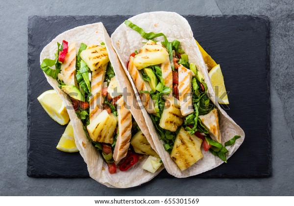 Chicken tacos with grilled pineapple\
and vegetables. Mexican fast food. Street tacos with barbecue\
chicken and pineapple on slate board.  Top view, copy\
space