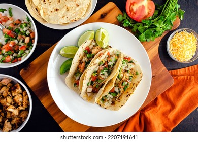 Chicken Tacos Topped with Pico de Gallo and Cheese: Three tacos on a plate surrounded with toppings and tortillas - Powered by Shutterstock