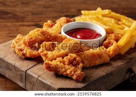 Chicken tenders, battered and fried crispy wedges, with a bbq sauce and potato, on a dark rustic wooden table