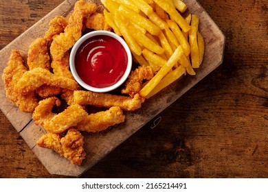 Chicken Tenders, Crispy Boneless Meat Pieces, With A Red Dip And French Fries, Overhead Flat Lay Shot On A Wooden Background With A Place For Text