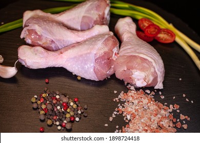 Chicken thighs pink salt, black pepper, pink pepper, white pepper, greens, tomatoes on a black board.