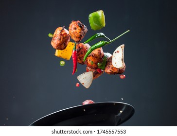 Chicken Tikka Kebab floats up in the air above the silver metal plate.