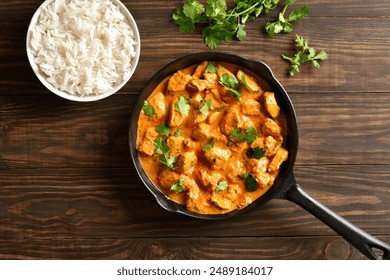 Chicken tikka masala curry in cast iron pan and bowl of rice on wooden background. Traditional indian dish. Top view, flat lay, close up - Powered by Shutterstock