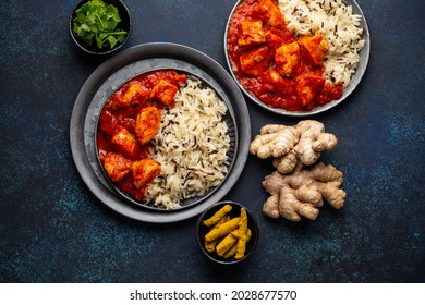 Chicken tikka masala dish with rice, flat Indian bread and spices in rustic metal plates on concrete background top view. Chicken tomato curry, turmeric root, fresh cilantro, traditional Indian meal 