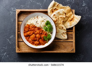 Chicken tikka masala spicy curry meat food with rice and fresh naan bread in wooden tray on black stone background