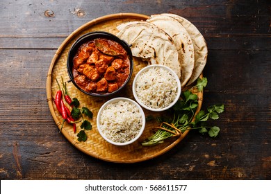 Chicken tikka masala spicy curry meat food in cast iron pot with rice and naan bread on wooden background