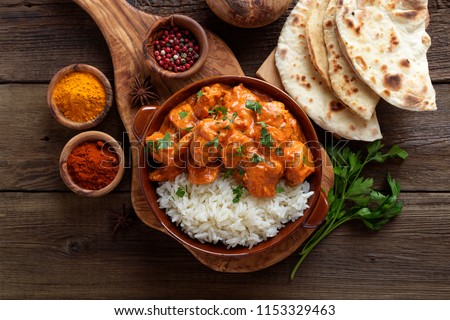 Chicken tikka masala spicy curry meat food in a clay plate with rice and naan bread on wooden background.