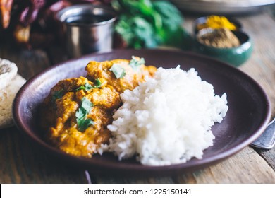 Chicken Tikka Masala (traditional indian curry) with rice and indian bread chapati decorated with spicy red chili peppers, cilantro, Indian spices (turmeric, garam masala) on an old wooden table