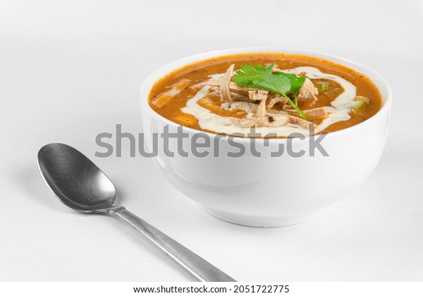 Chicken tortilla soup with fried strips\
of corn tortillas. Mexican soup on white\
background
