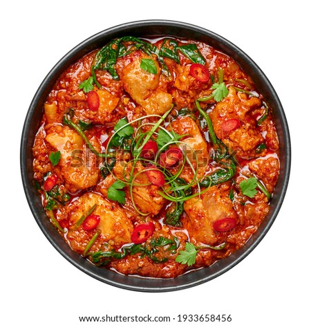 Chicken Vindaloo with spinach in black bowl isolated on white. Indian cuisine meat chilli curry dish. Authentic asian food.