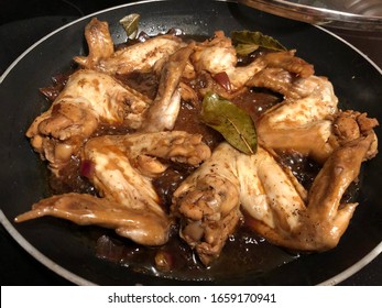 Chicken wings cooked adobo style in a pan, with bay leaves